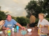 Buitenterras van de Geckobar op de achtergond, regenboog, uitzicht en Daniel, de Ngo worker uit SenMonorm en (zo bleek laat op de avond) ex-kindsoldaat uit Uganda. Aan tafel Jolanda met de grote Alcohol Australier met het kleine hartje